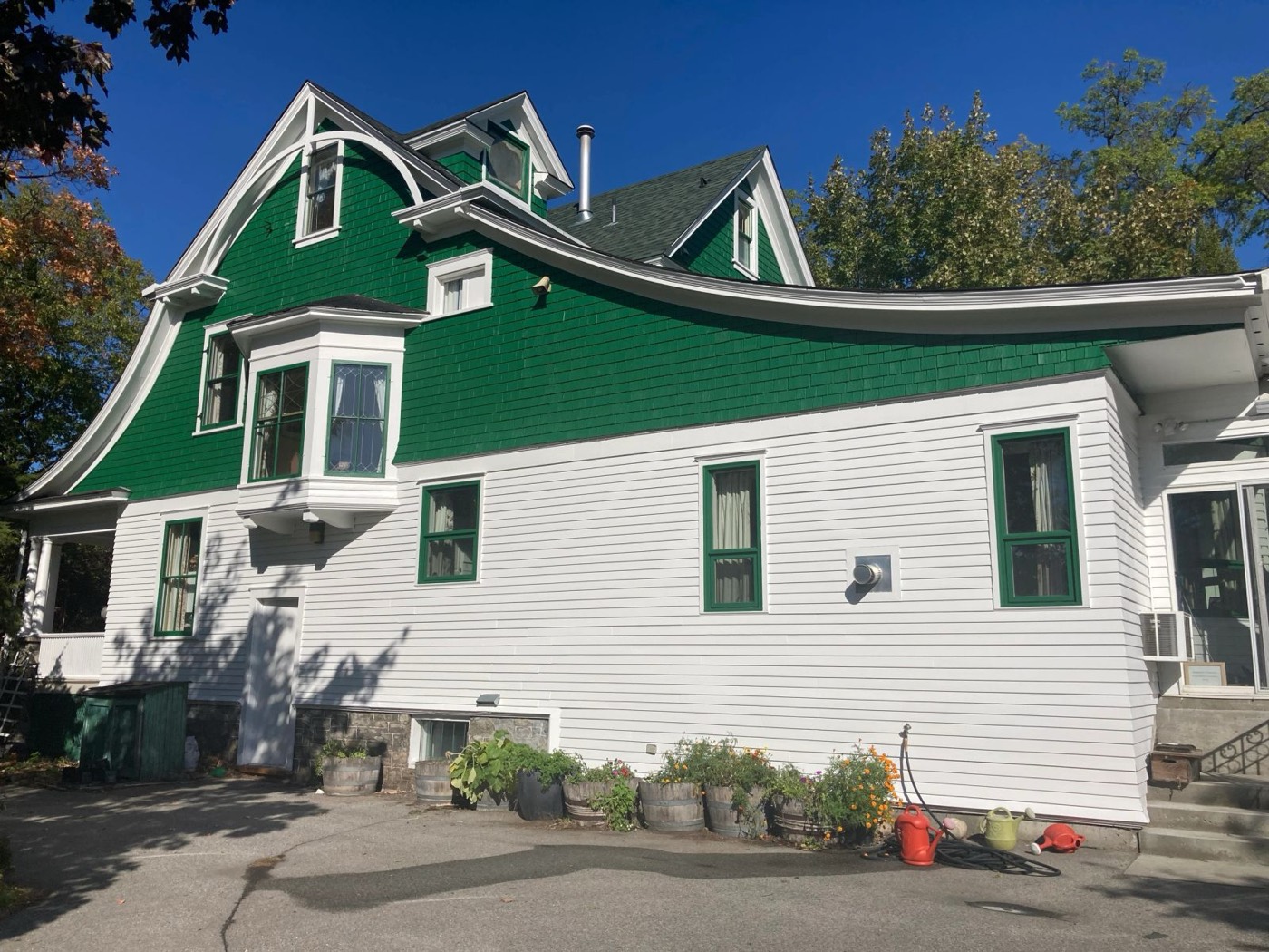 Green-shingled heritage house exterior being repainted, ladders against the gable